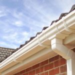 UPVC Guttering with white plastic rain gutter and downpipe attached to roof edge of brick house.